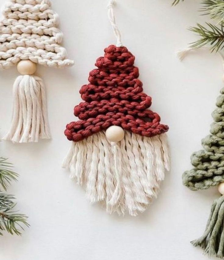 three knitted christmas trees hanging from the side of a white wall next to pine branches