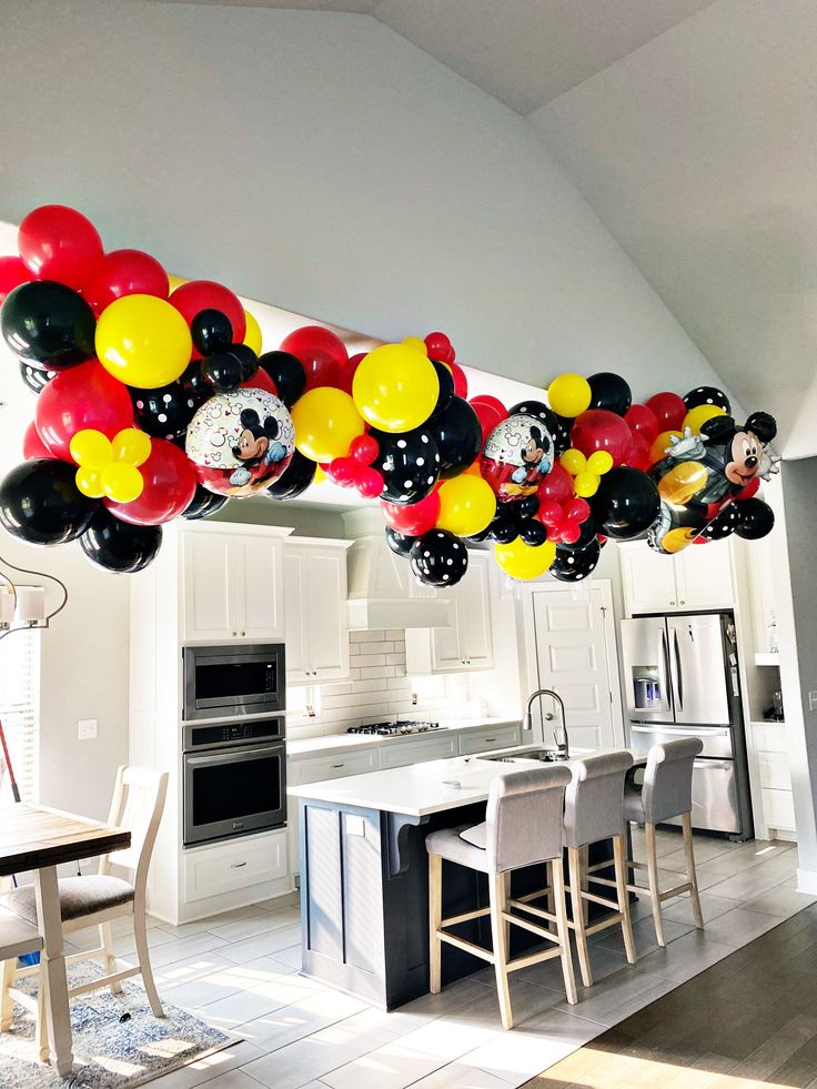 mickey mouse balloons are hanging from the ceiling in a kitchen with an island and dining table