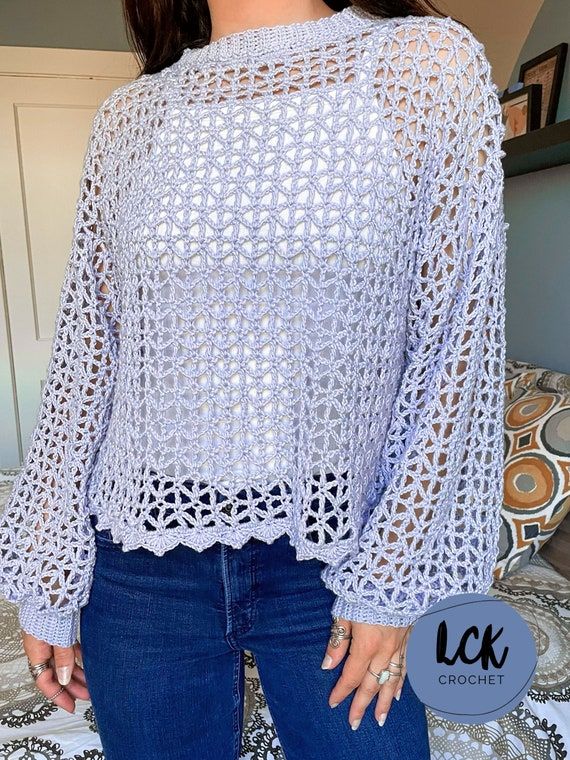 a woman standing in front of a bed wearing jeans and a white top with crochet