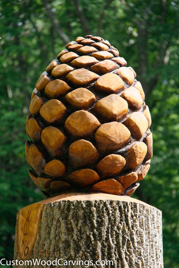 a carved pine cone sitting on top of a tree stump in front of some trees