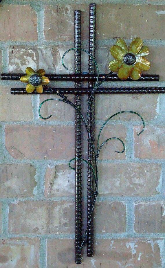 a metal cross with flowers on it against a brick wall