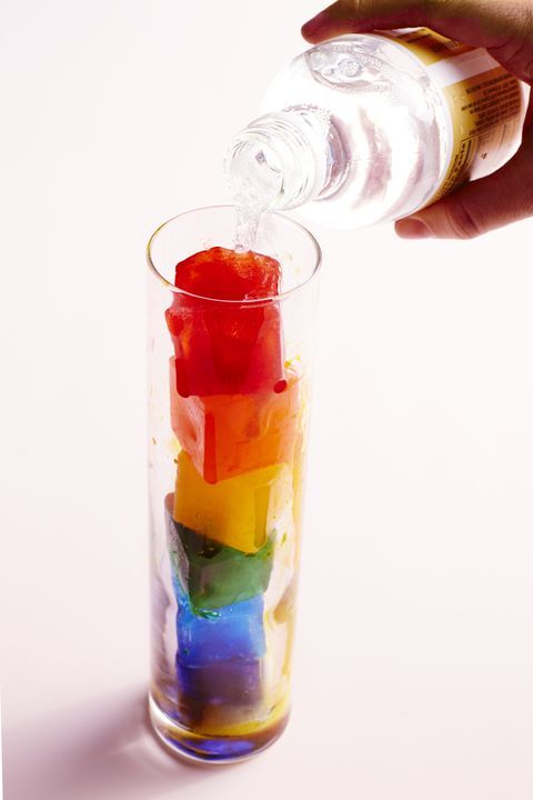 a person pouring water into a glass filled with colored ice cubes and rainbow liquid