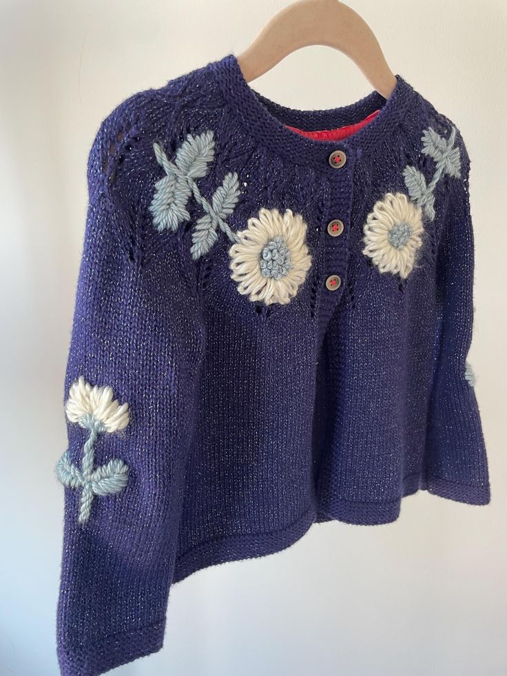 a blue sweater with flowers on it hanging from a wooden hanger