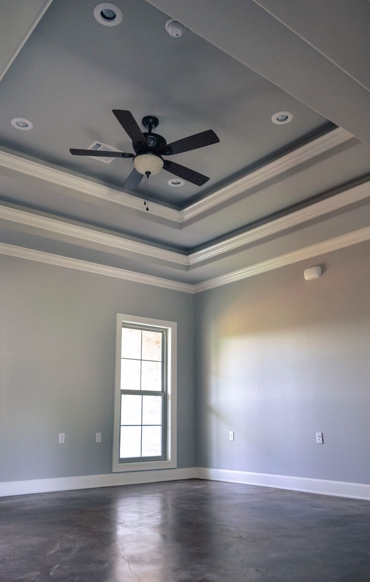 an empty room with a ceiling fan and two windows in the corner, all painted gray