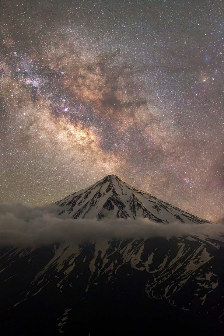 the night sky is filled with stars and clouds over a mountain covered in snow as seen from below