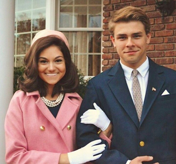 a man and woman standing next to each other in front of a brick building wearing white gloves