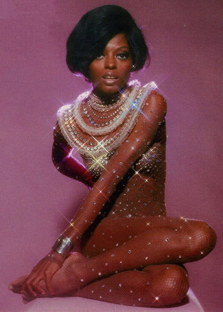 a woman sitting on top of a white stool wearing a dress and pearls around her neck