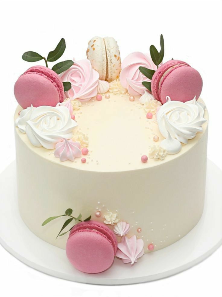 a white cake with pink and white frosting decorated with macaroons on top