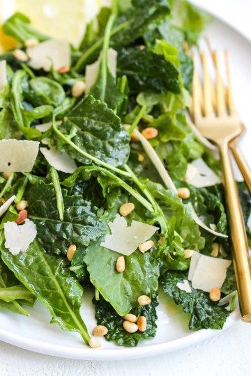 a white plate topped with salad and gold utensils next to lemon wedges