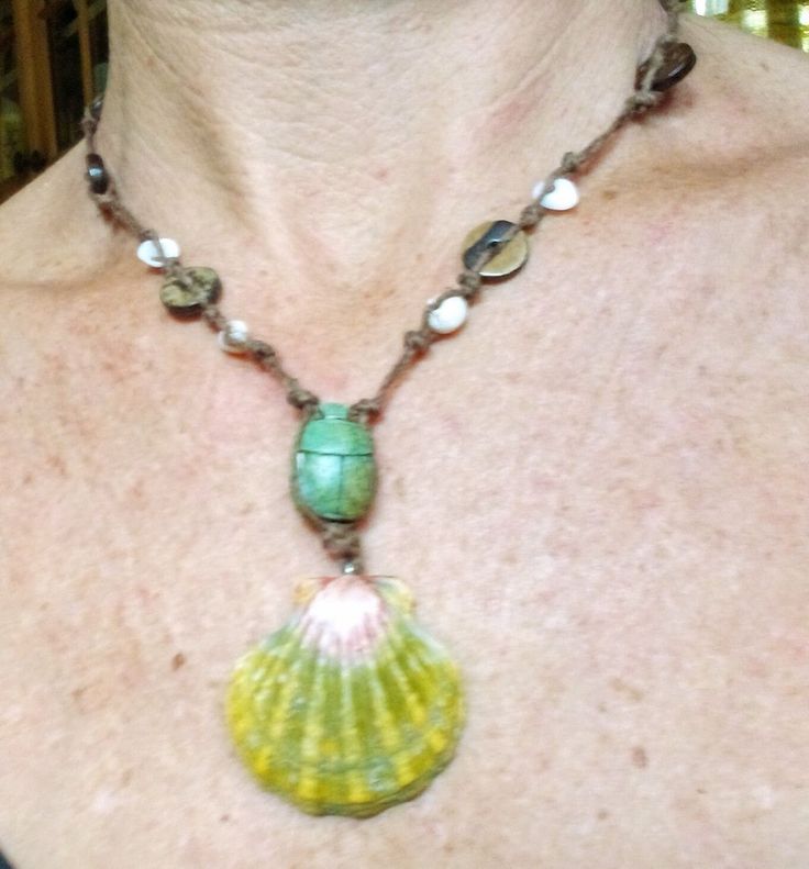 a woman wearing a necklace with a green shell on it's side and beads around the neck