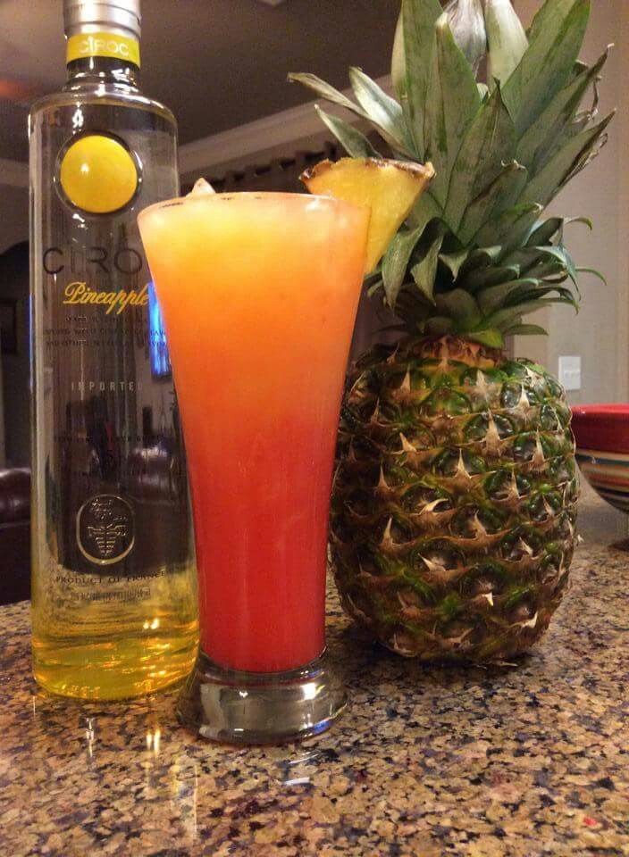 a pineapple drink next to a bottle of booze and a pineapple on the counter