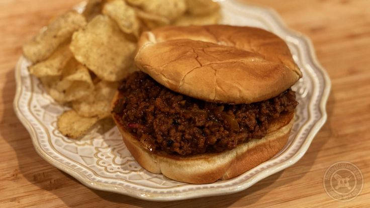 a plate with a sloppy joe and chips on it, sitting on a wooden table