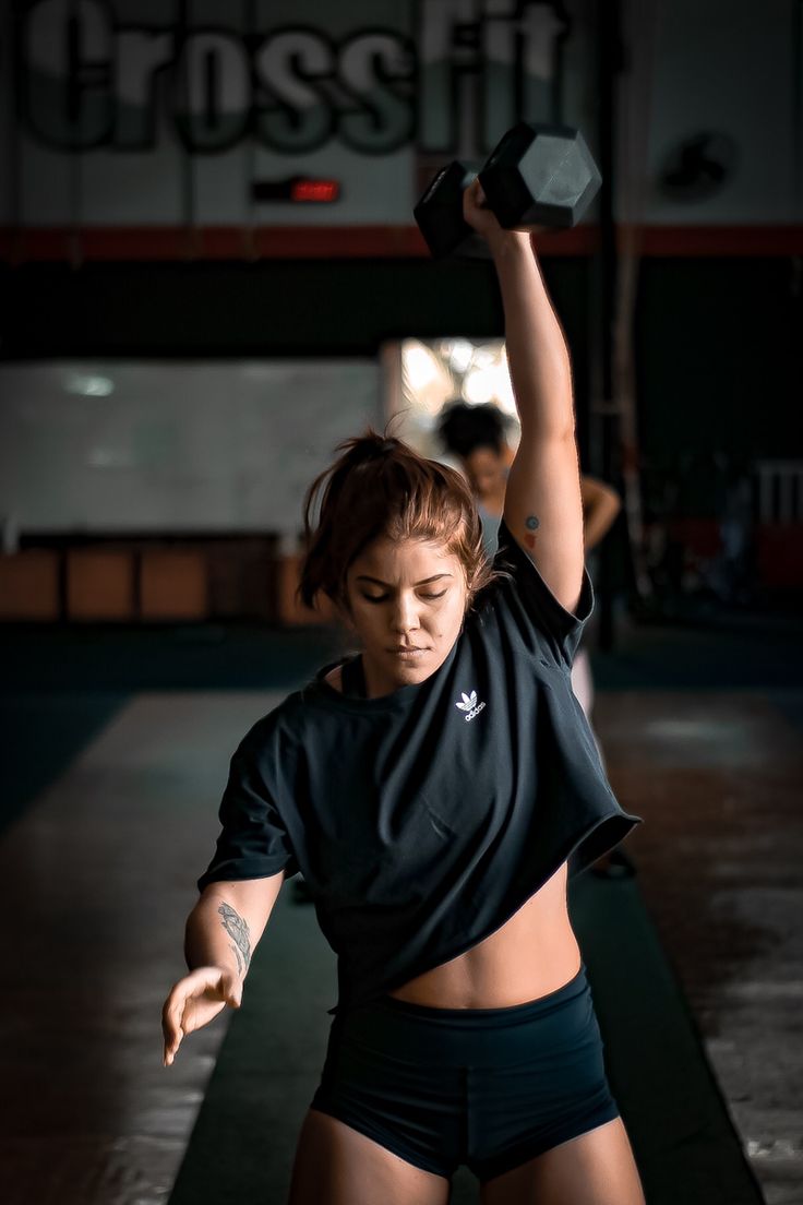 a woman holding two dumbs while standing in front of a crossfit sign