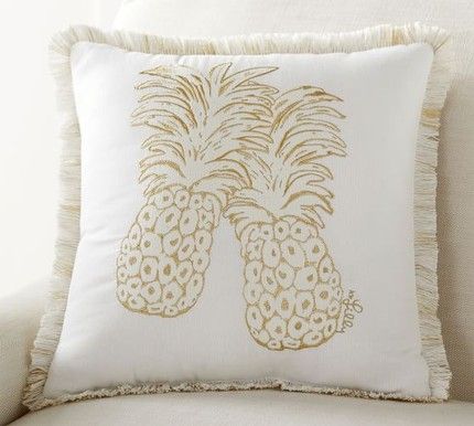 a white pillow with gold pineapples printed on the front and back, sitting on a couch