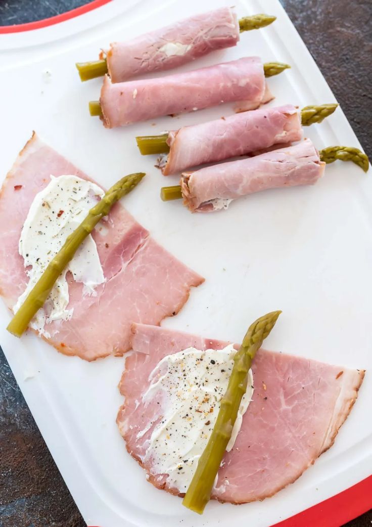 ham and asparagus wrapped in cheese on a white platter with pickles