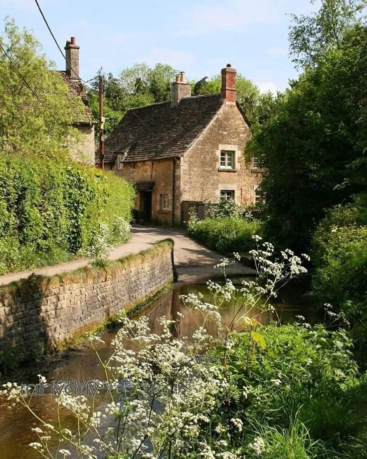 an old stone house sitting next to a river in the middle of a lush green forest