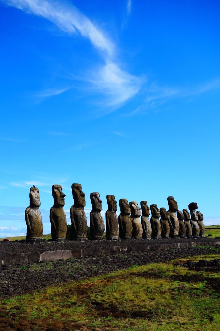 the moai statues are lined up in a row, against a blue sky with wispy clouds