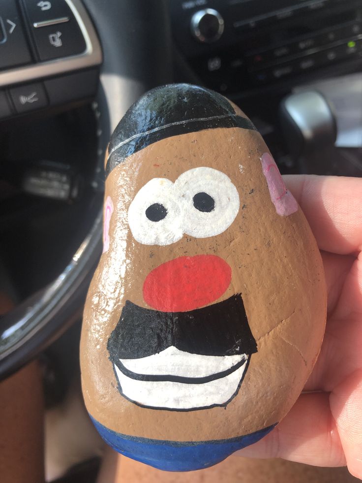 a hand holding a rock with a face painted on it in front of a car steering wheel