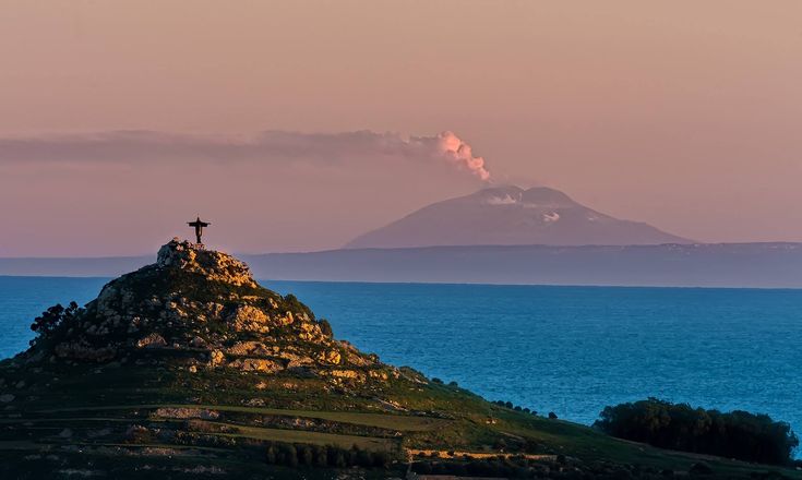 an island with a cross on it in the middle of the ocean and a mountain behind it