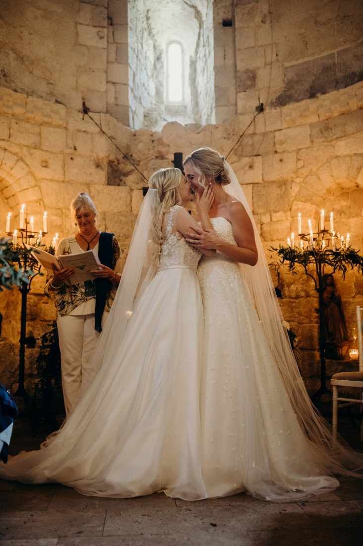 two women in wedding gowns standing next to each other at a alter with candles