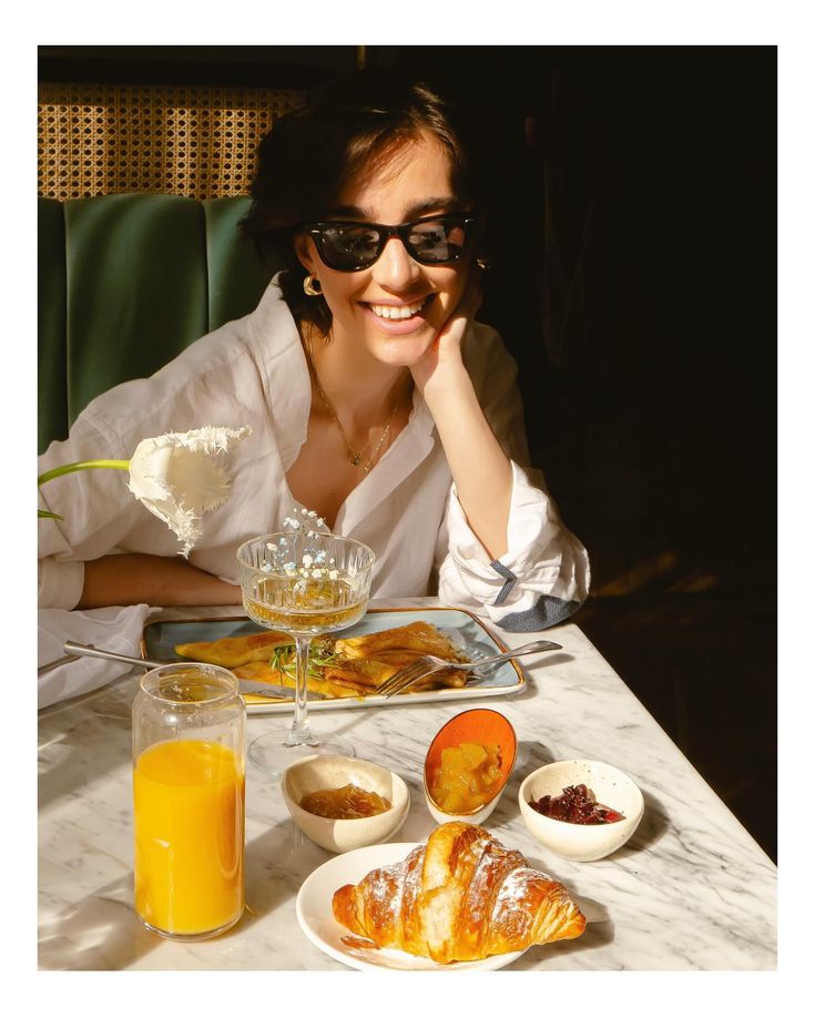 a woman wearing sunglasses sitting at a table with food and drinks in front of her