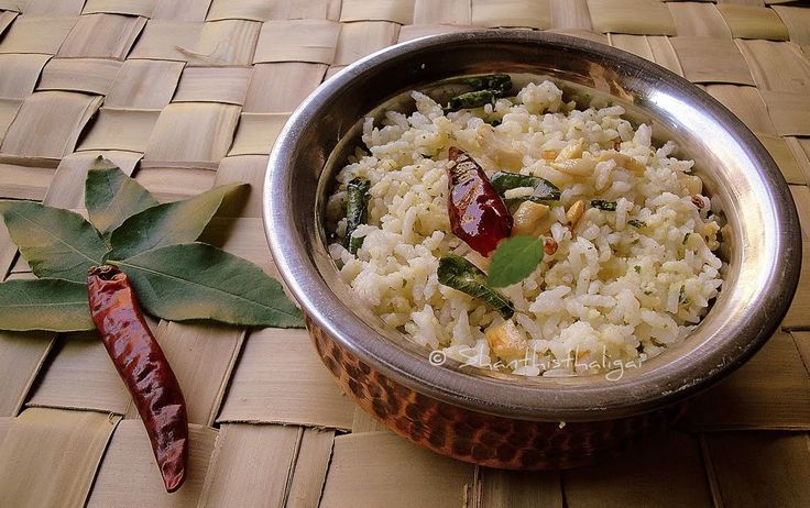 a metal bowl filled with rice and vegetables next to a leaf on a woven mat