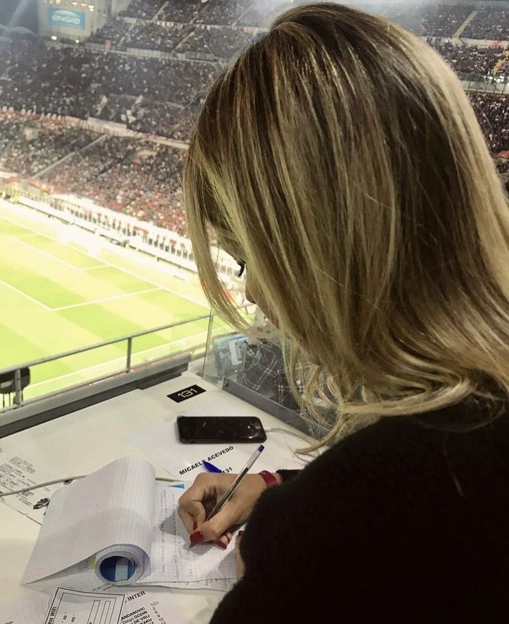 a woman sitting at a table in front of a stadium filled with people and writing on paper