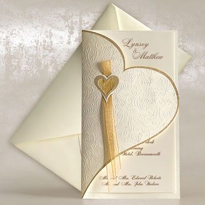 a white and gold wedding card with a heart on the front, an elegant ribbon in the middle