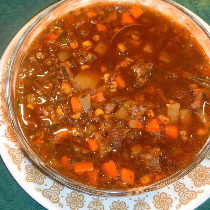 a bowl of soup with carrots and meat in it on a plate next to a spoon