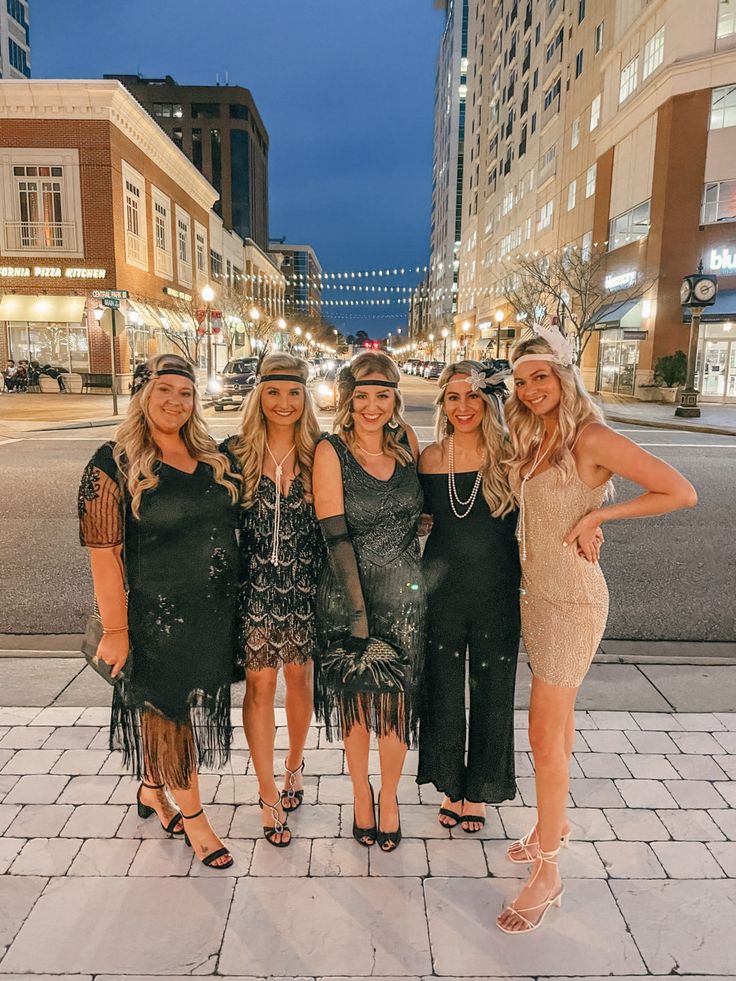 four beautiful women posing for a photo in front of the city street at night time