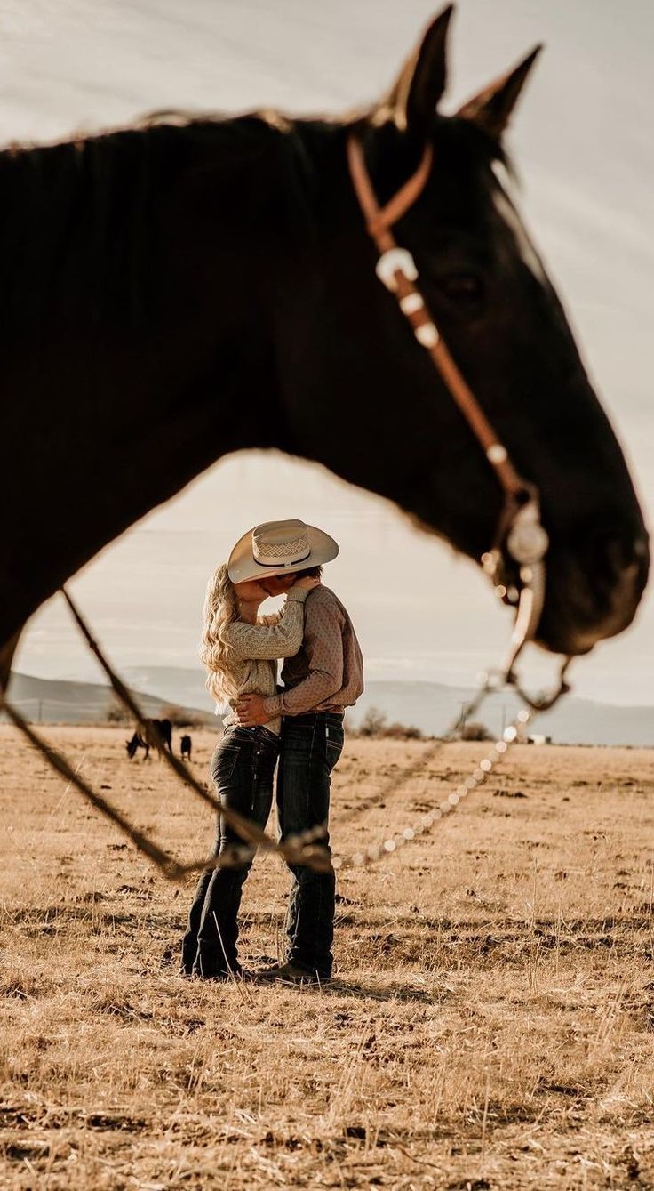 a man standing next to a brown horse on top of a dry grass covered field