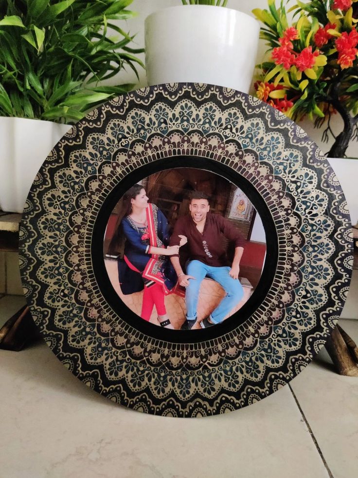 an ornate black and white photo frame with two women sitting on the floor in front of potted plants