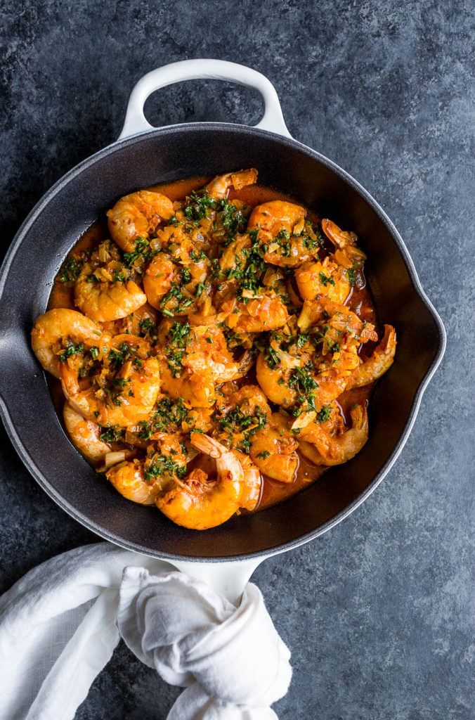 a skillet filled with shrimp and sauce on top of a white cloth next to a napkin