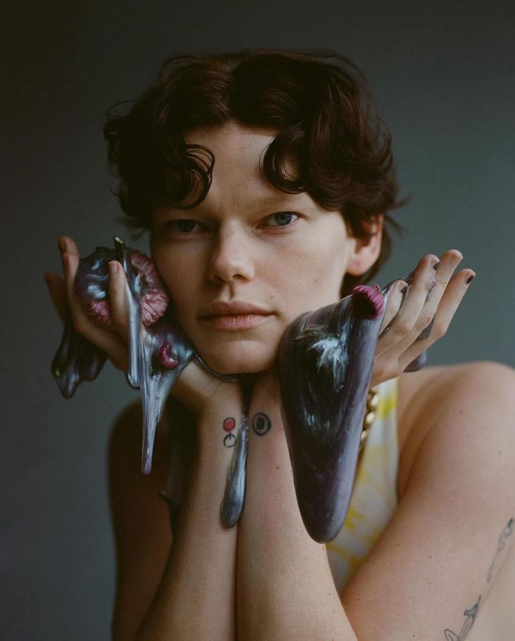 a woman with tattoos holding two birds on her chest and looking off to the side