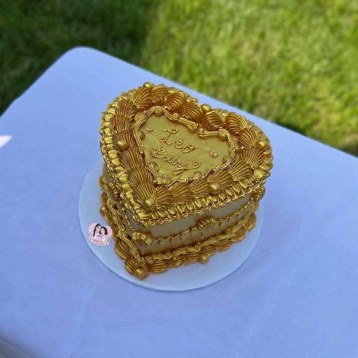 a heart shaped cake sitting on top of a blue tablecloth covered table with grass in the background