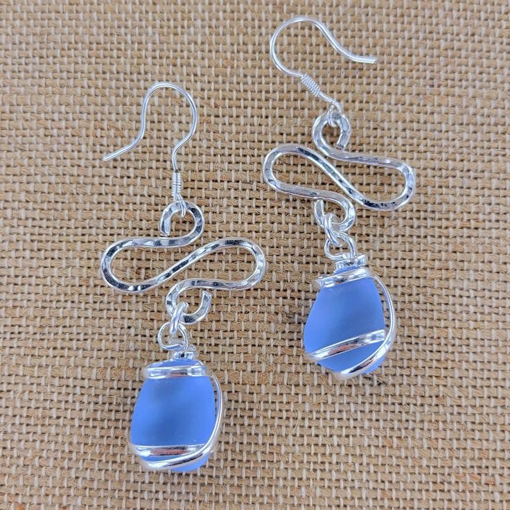 the earrings are made from glass and silver wire, with blue beads hanging from them