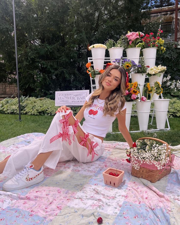 a young woman sitting on top of a blanket next to flowers and baskets filled with flowers