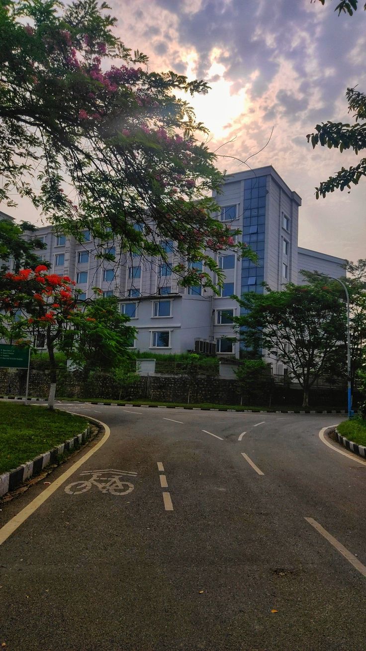 the sun is setting on an empty street in front of a building with trees and bushes