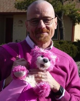 an older man holding a pink teddy bear in front of a house on a sunny day