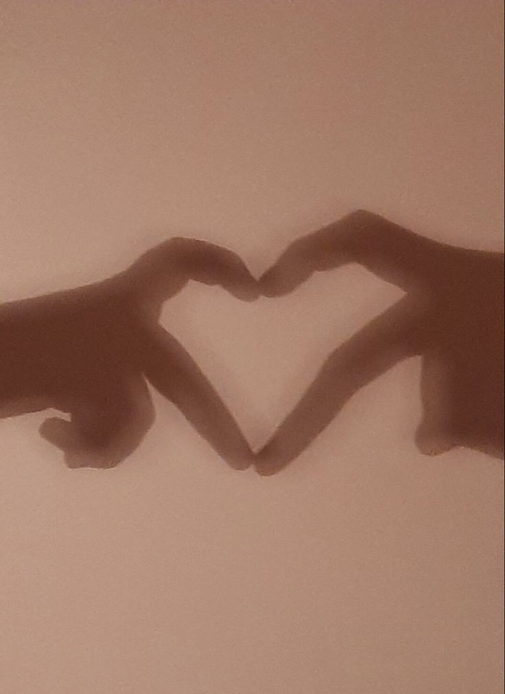 two hands making a heart shape in the middle of a wall with shadows on it