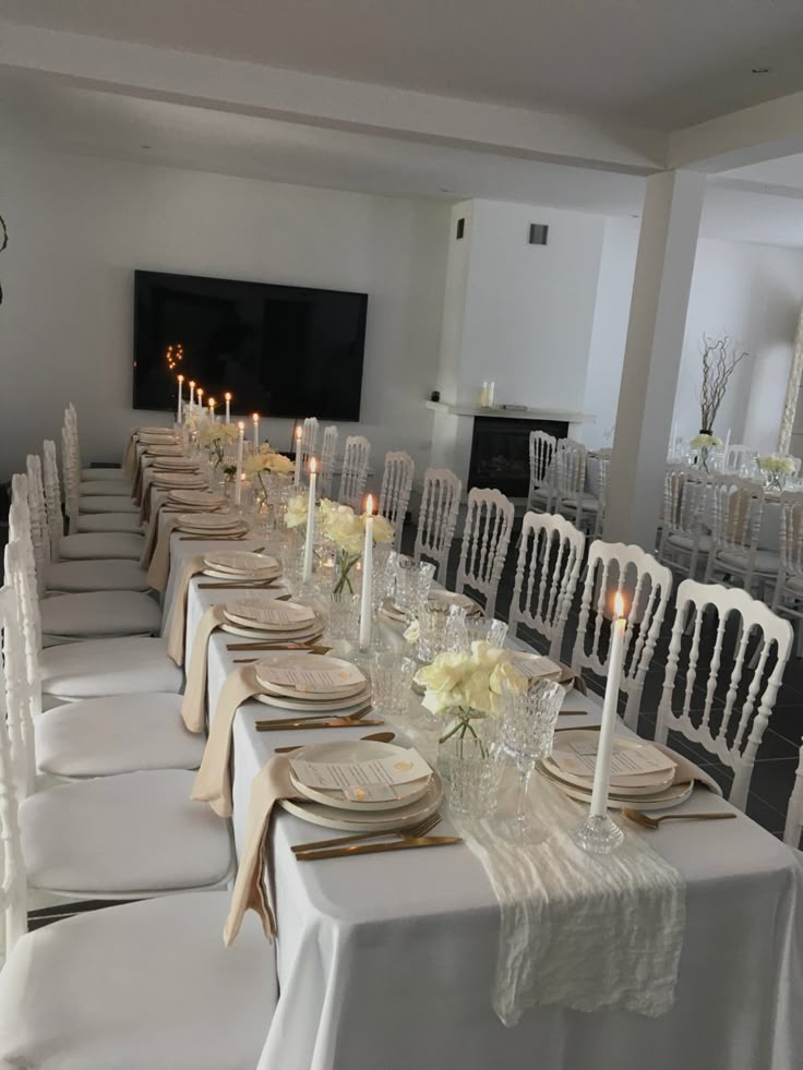 a long table is set with white chairs and candles