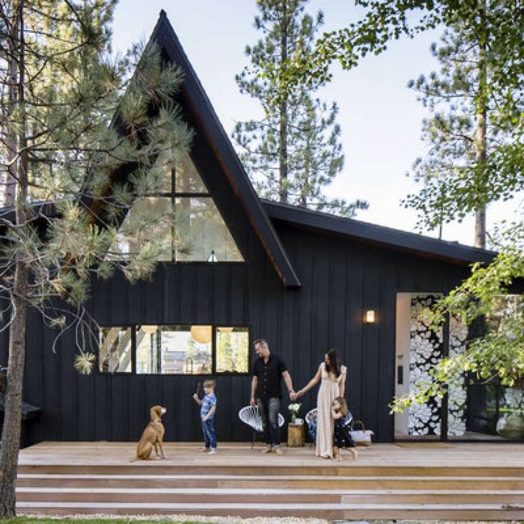 a family with two children and a dog are standing on the front porch of a black house