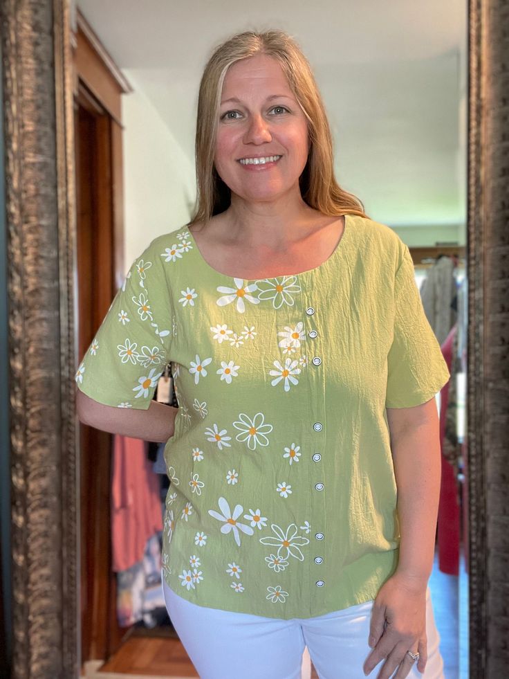 The Happy Daisy Top is a beautiful linen top with a fun daisy pattern. Looks great with white bottoms. It has zero stretch. Jessica is wear a L and was a bit worried about it being tight in the arms. You could go up a size for a more relaxed fit. Faux Button Front Spring Linen Floral Print Tops, Spring Floral Print Linen Tops, Summer Floral Linen Top, Casual Linen Tops With Floral Print, Spring Cotton Daisy Print Tops, Spring Daisy Print Cotton Tops, White Daisy Print Tops For Spring, Cotton Daisy Print Tops For Spring, Casual Daisy Print Top For Summer