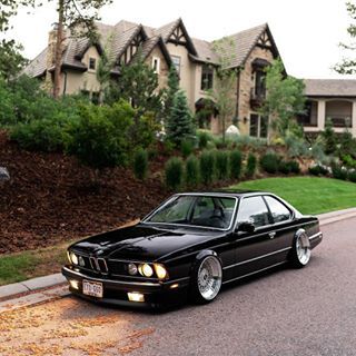 a black bmw is parked on the side of the road in front of a house