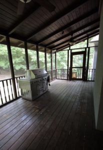 an outdoor covered porch with grills and tables on the outside deck, surrounded by wood flooring