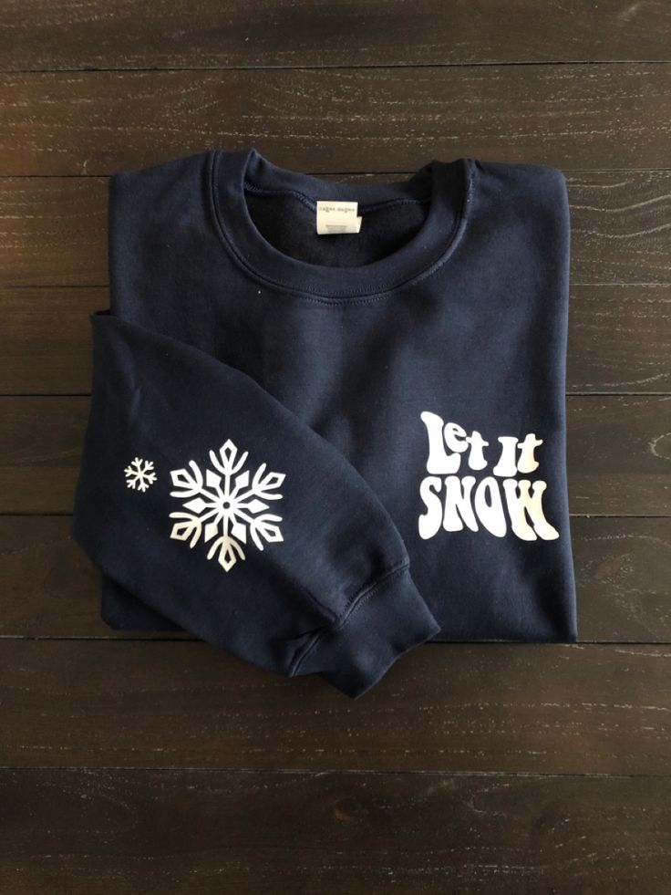 two sweatshirts with the words let it snow printed on them sitting on top of a wooden floor