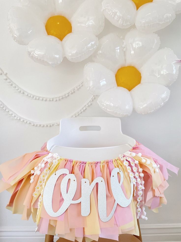 a table topped with white balloons and pink and yellow ruffled skirt under an air filled balloon