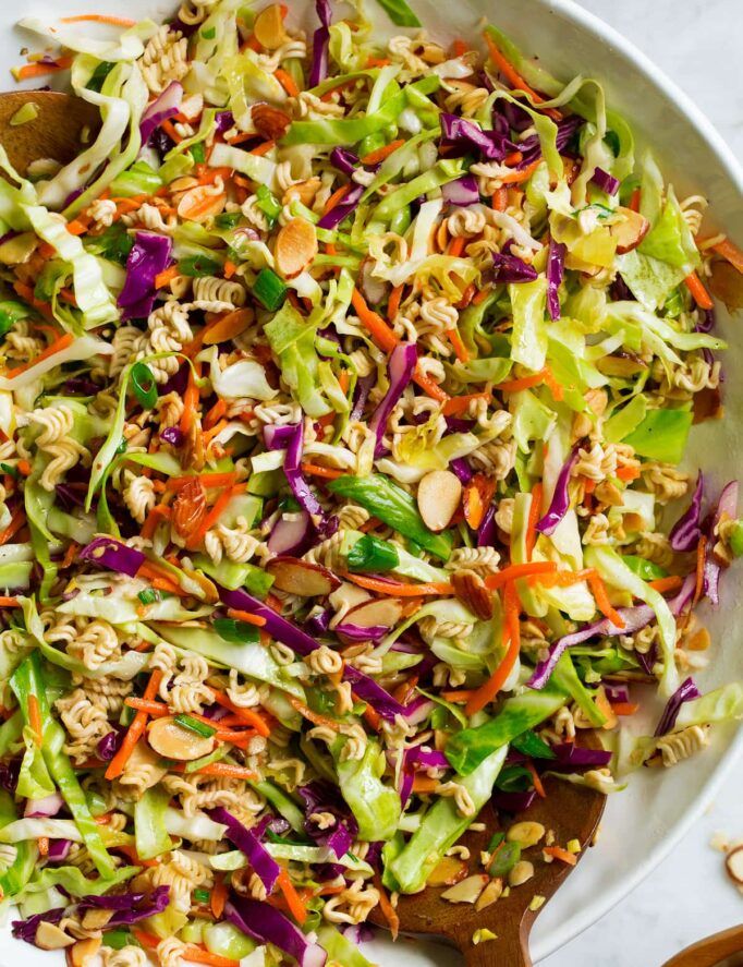 a white bowl filled with coleslaw slaw next to two wooden spoons