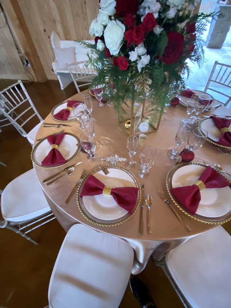 the table is set with red and white napkins, gold place settings, and flowers