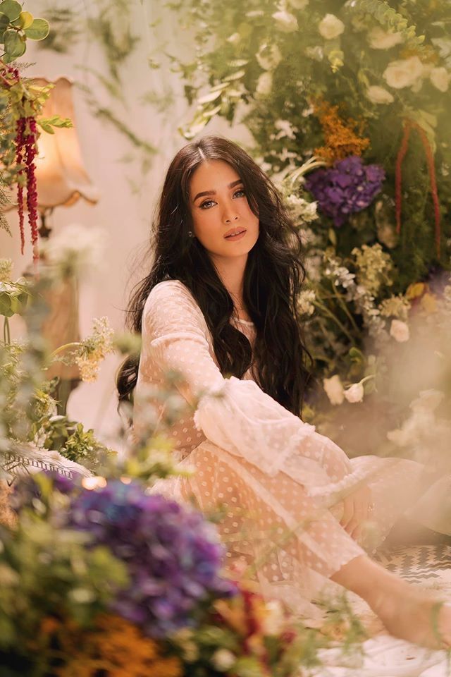 a woman sitting on the ground surrounded by flowers and plants, posing for a photo